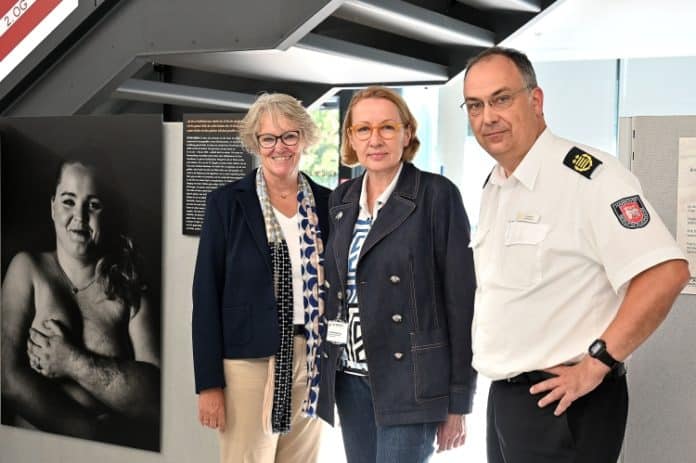 Feuerwehr holt Wanderausstellung „Ein Teil von mir – Narben machen (k)einen Unterschied“ nach Hannover - Susanne Falk, Dr. Mechthild Sinnig und Christoph Bahlmann vor Porträt eines „Paulinchen-Kindes“